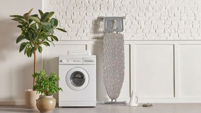 Best washing machines - a washer in the center of a room with a sink to the right and a tree and chair on the left