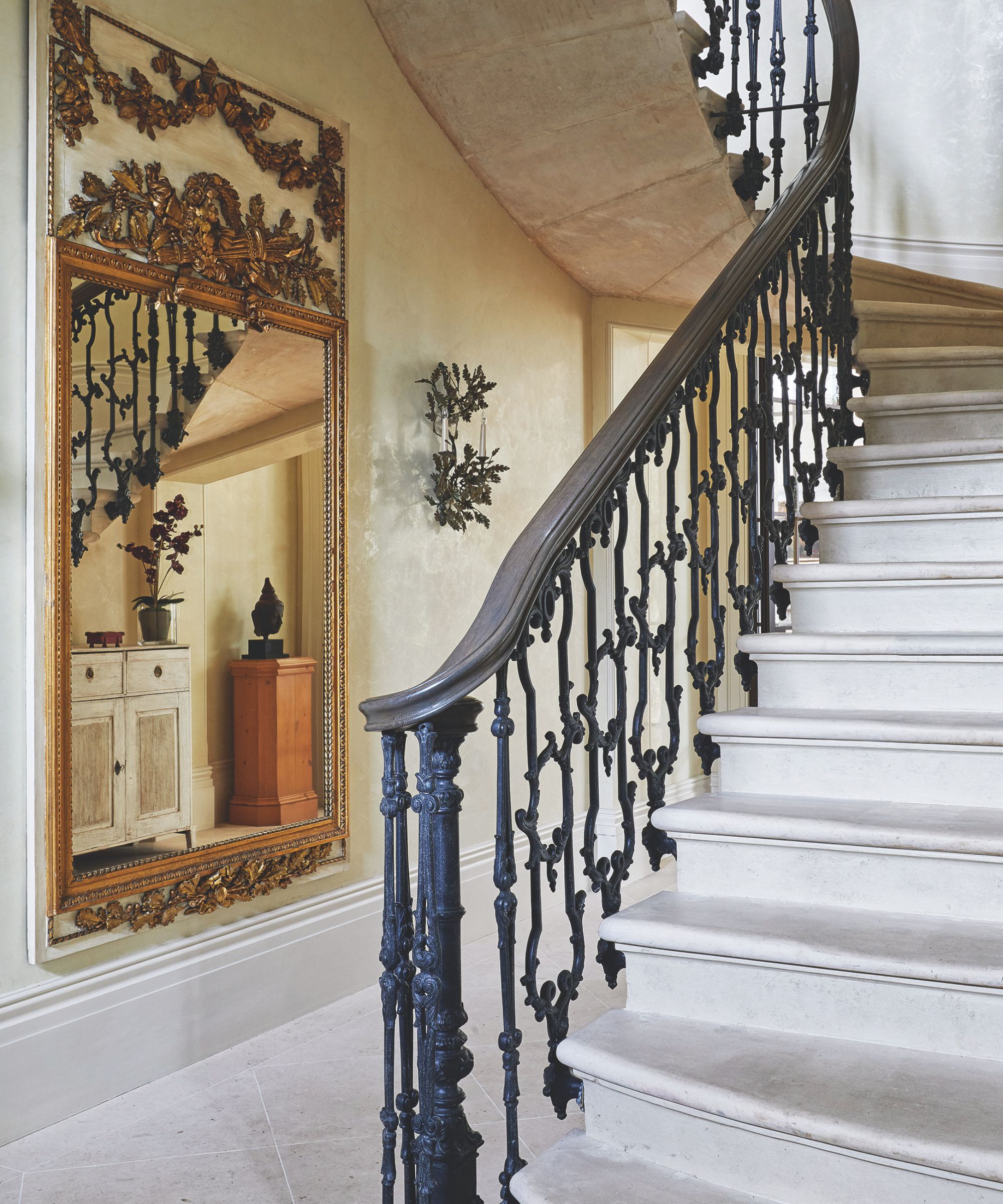 Hallway with stone floors and staircase, ornate gold mirror, sconce and wrought iron railing