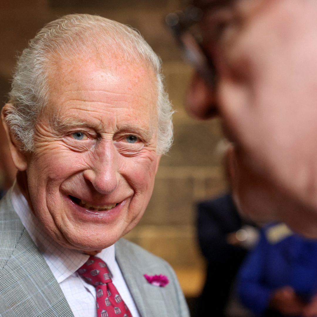 King Charles in a gray suit smiling at a D-Day veteran