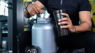 Close up shot of bodybuilder hands taking protein powder and mixing with water on bottle by shaking at gym - concept of muscular gain, nutritional supplement and wellness