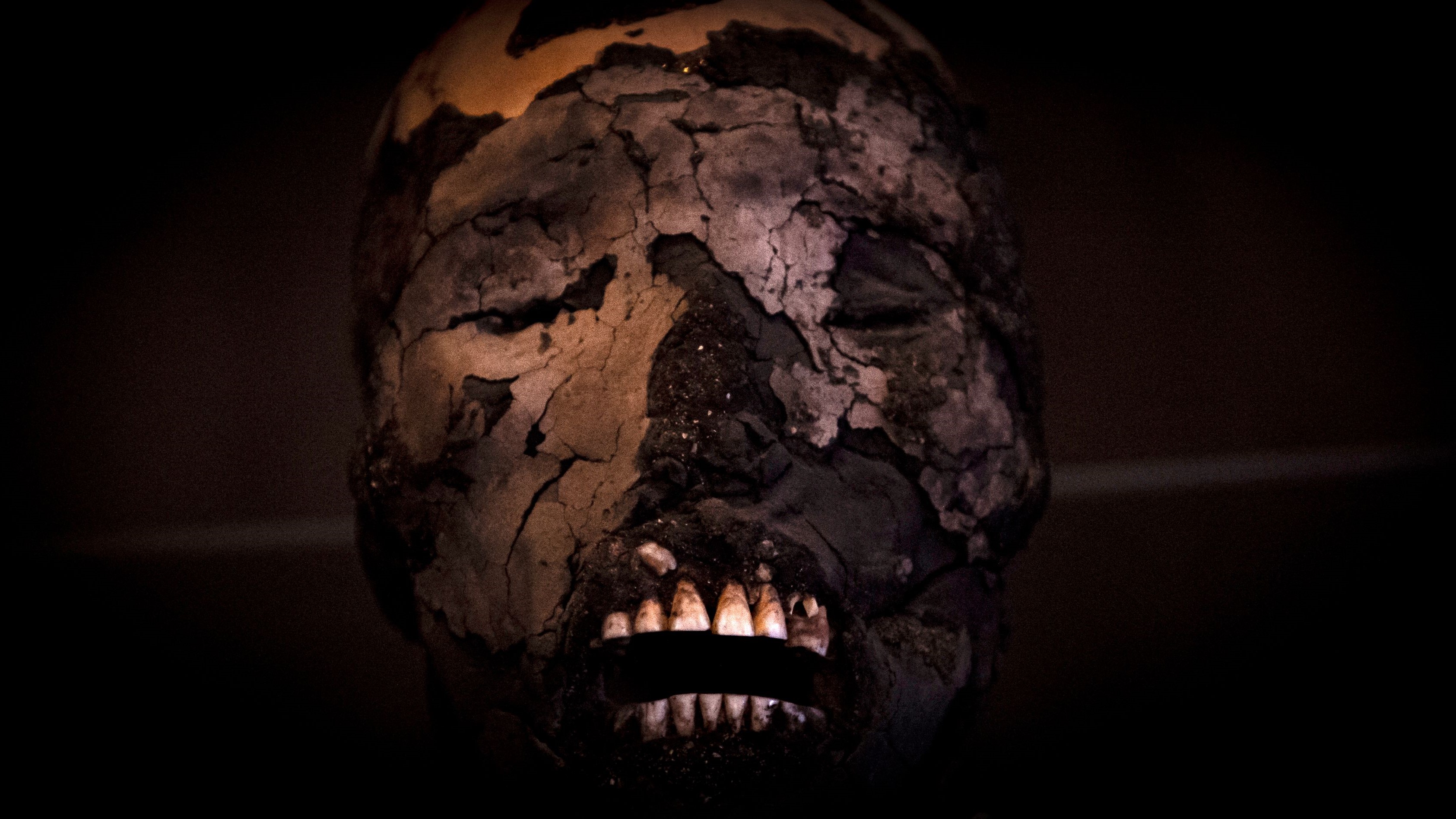 A Chinchorro mummy's face with teeth showing on a dark background