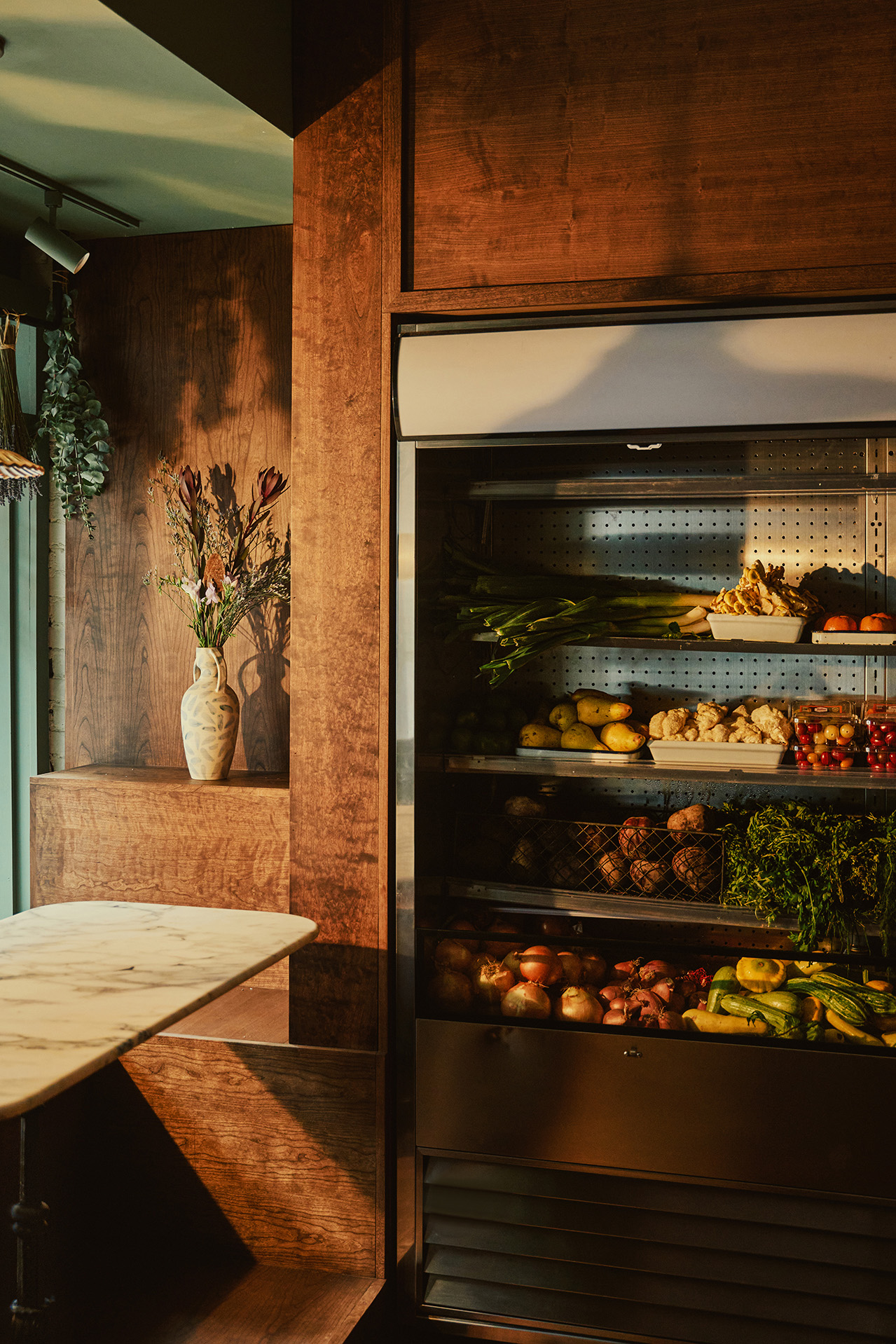Interior shots of a brick, wood, and marble-clad cafe, bakery, and butcher, decorated with modern rustix furnishings and floral wallpaper.