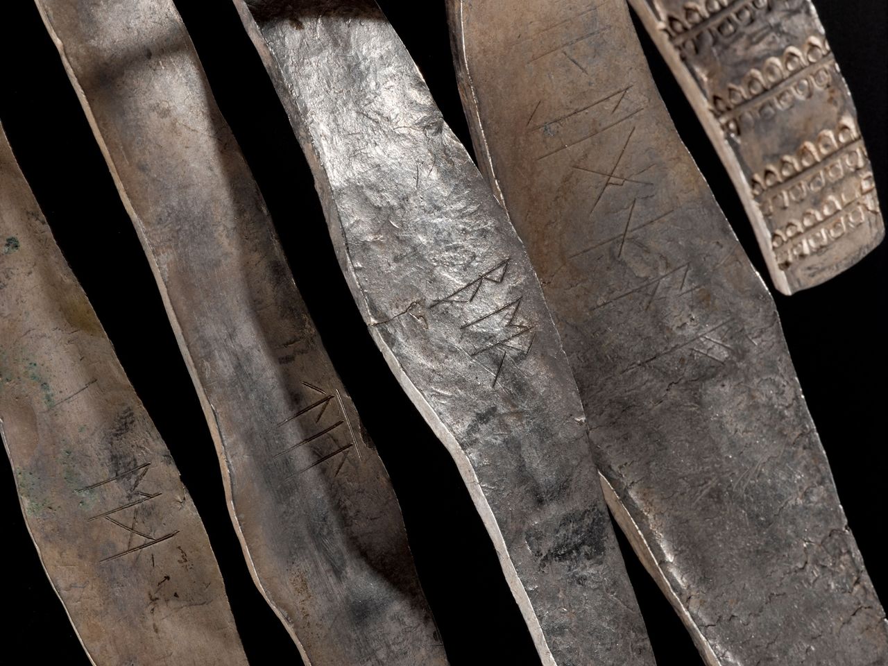 a close-up of multiple silver armbands with runic inscriptions