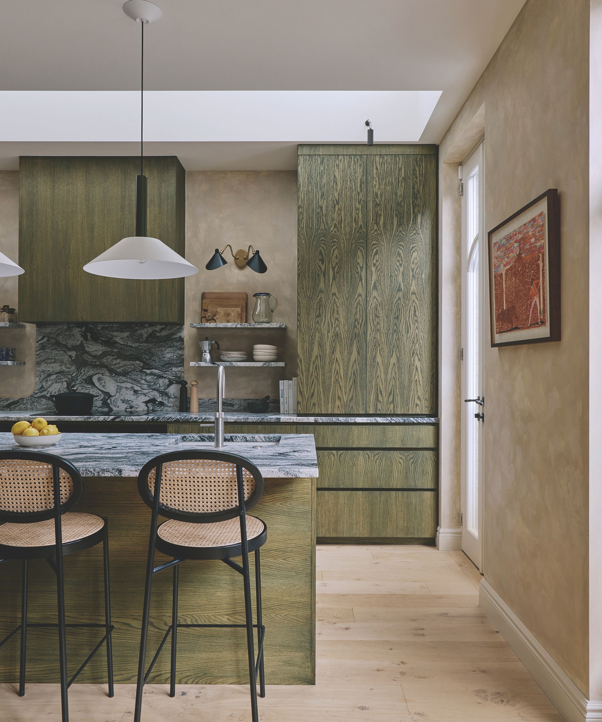 Modern kitchen featuring olive green wood grain cabinets, dark veined marble countertops, skylight, pendant light, and woven cane barstools
