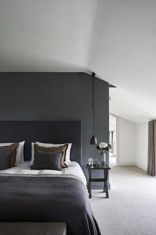 bedroom with white walls, one black feature wall, black bed, white bedlinen, wooden side table, oatmeal floor, pendant light