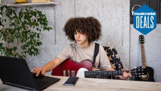 A young boy uses a laptop while learning to play electric guitar