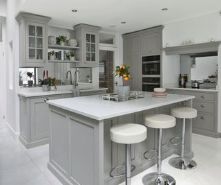 kitchen with grey painted cabinets and 4 white stools in front of an island unit