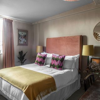 Bedroom with double bed with pink statement headboard and mustard throw