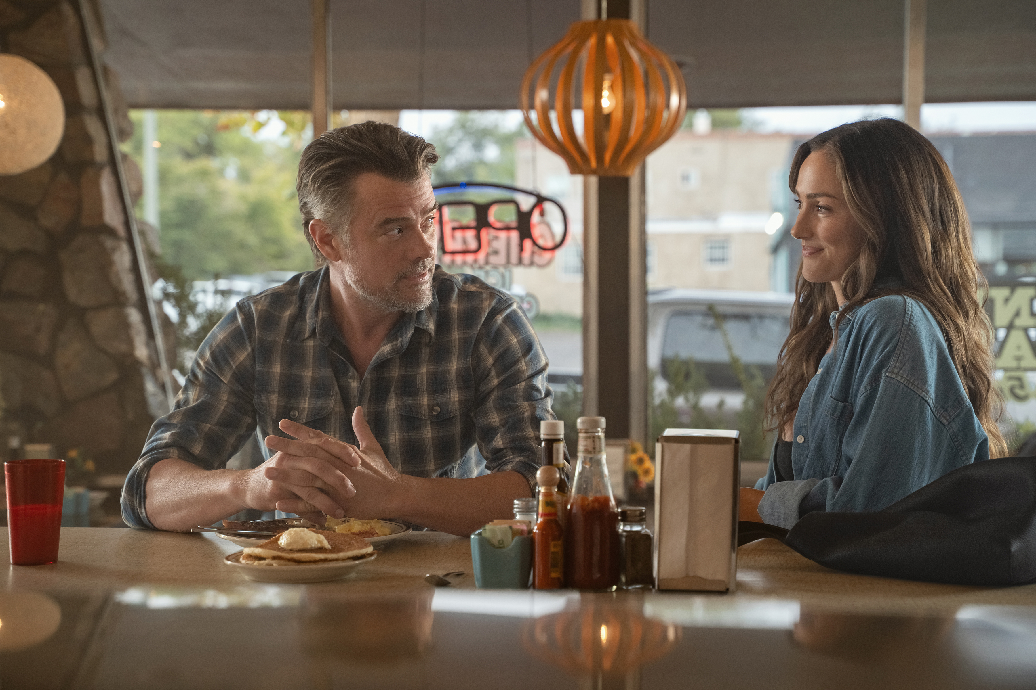 Josh Duhamel as Staten and Minka Kelly as Quinn sitting in a diner talking over pancakes in a still from ransom canyon season 2