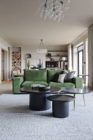 A large open plan sitting room / dining room with green velvet sofa, dining table and a built-in wood stack.