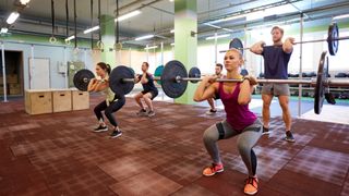 Group of people perform barbell thruster