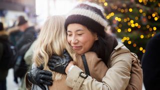 Two women hugging at a train station with sparkling Christmas tree behind them