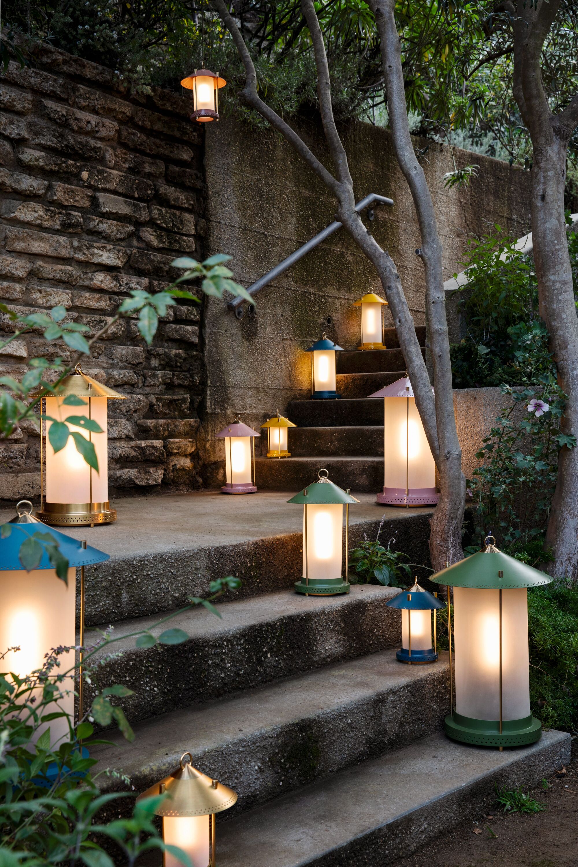 Image of a large, concrete outdoor staircase with plants growing around it and a lot of colorful lanterns in various sizes lining the stairs.