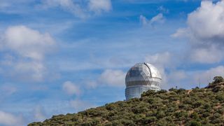 Hobby Eberly telescope dome sits on a hill with blue skies and clouds above.