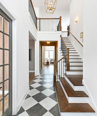 A white entryway with a dark wooden and white staircase, white walls, gray doors, and a dark gray and white marble checkerboard floor