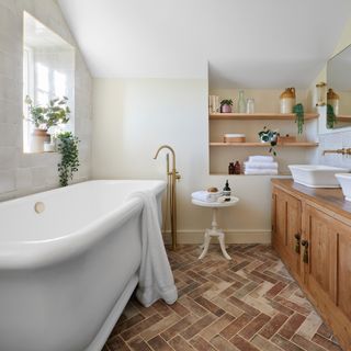 bathroom with large traditional bath tub, twin basin vanity unit, mirror, open shelving, and terracotta floor tiles