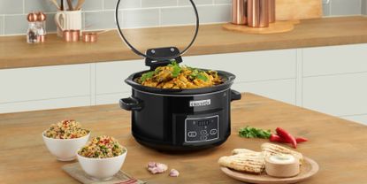 Crockpot black slow cooker on wooden kitchen bench with curry and rice being served