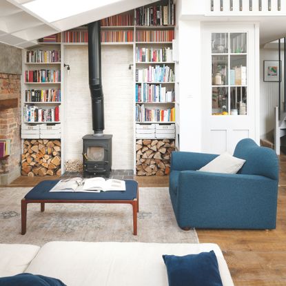 Living room with fitted shelves and a woodburner on the back wall, and a blue accent chair with matching coffee table