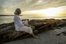 Senior woman sitting with her dog on a beach at sunset