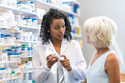 A pharmacist is holding a bottle of pills and assisting a customer with a question about medication.
