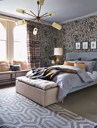 An example of bedroom chandelier ideas showing a gray bed and a gray and white patterned rug under a sputnik chandelier