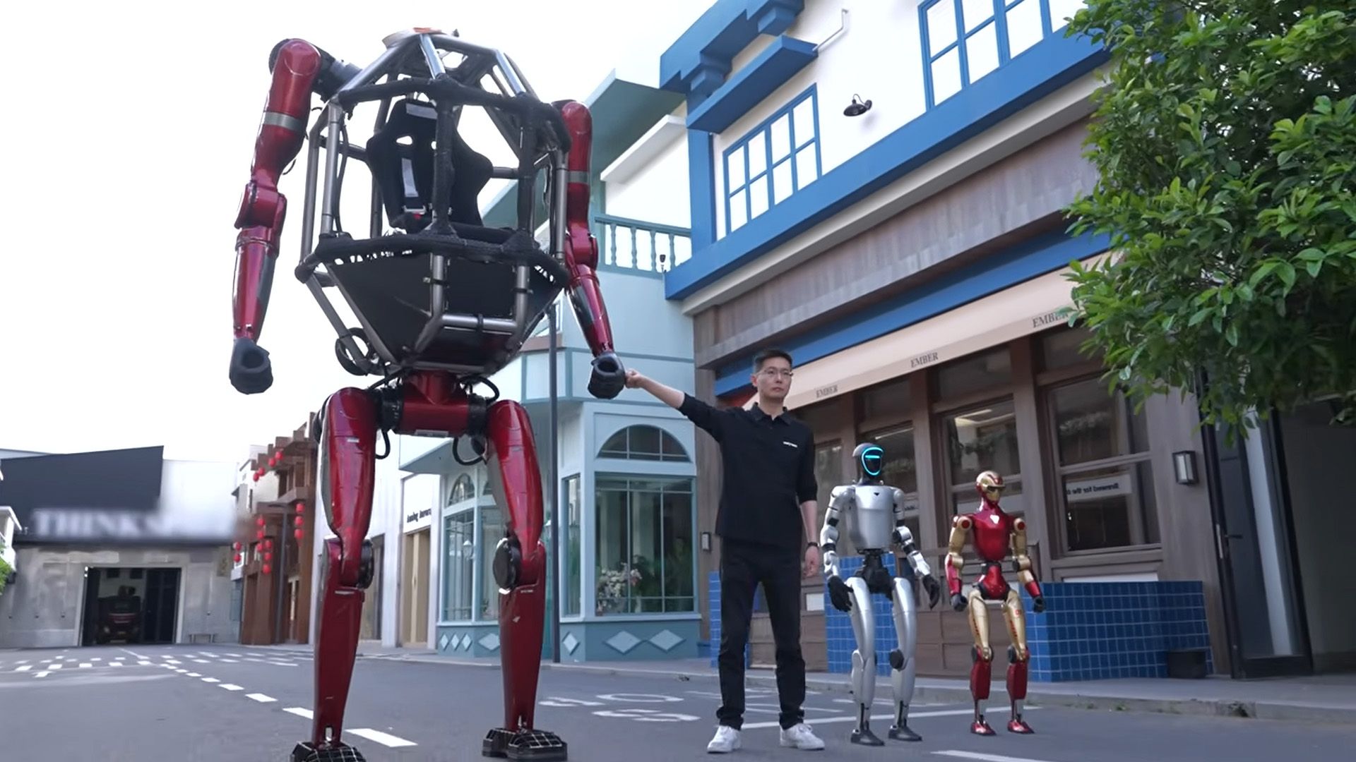 A man stands next to a series of robots, where he holds the hand of a large cage on a bipedal robot.