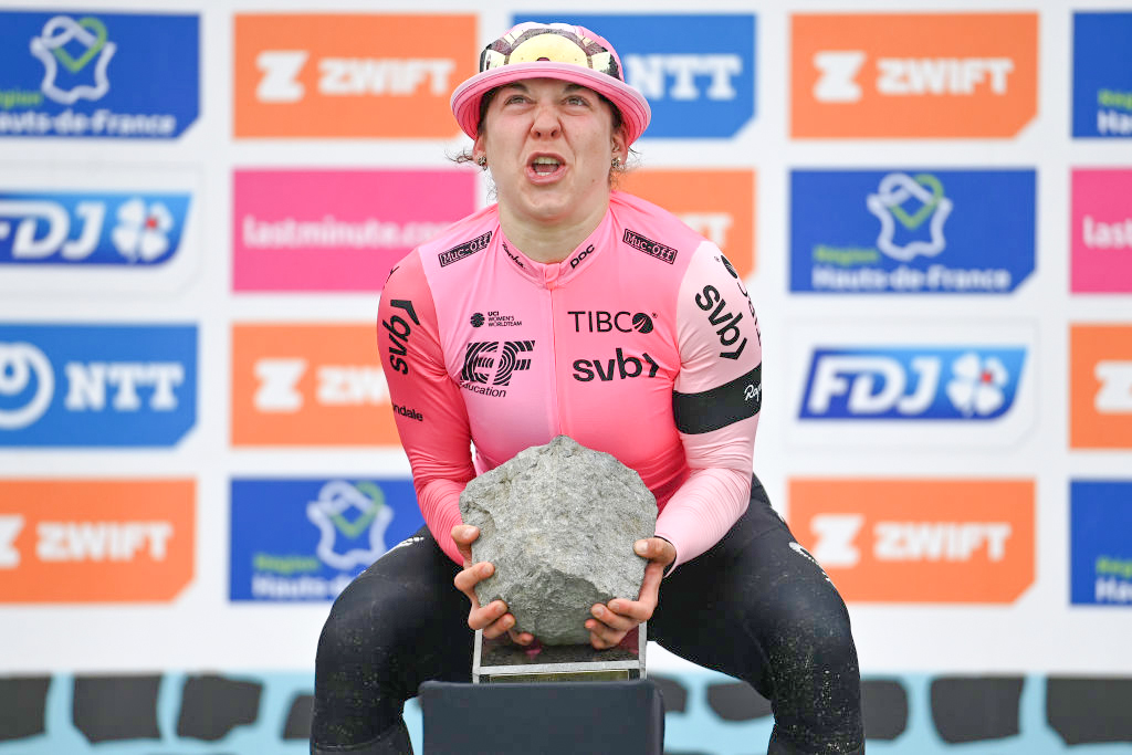 Alison Jackson hauls up the cobblestone trophy on the podium of the 2023 Paris-Roubaix Femmes