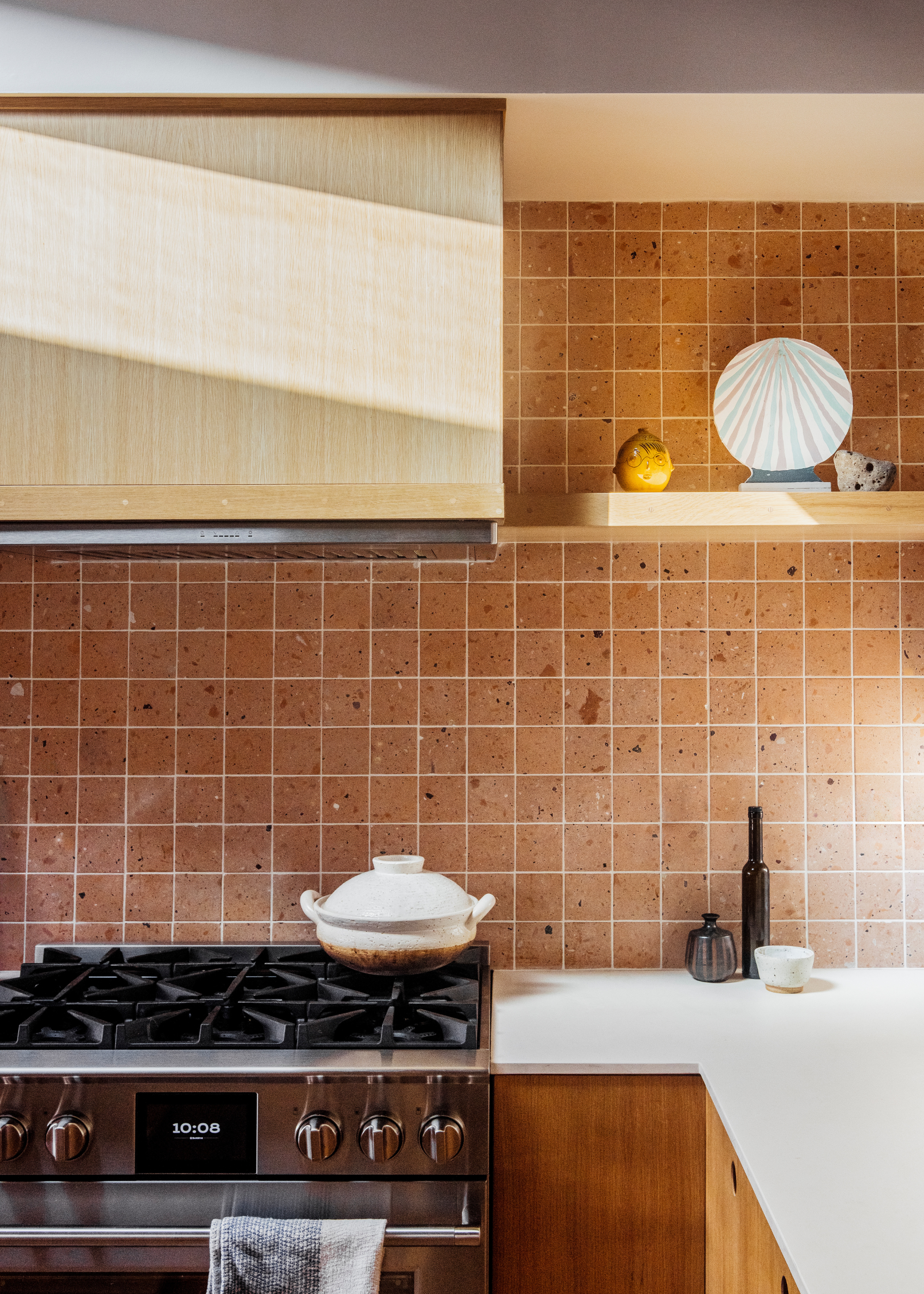 A kitchen with a terracotta style tiled backsplash and a view of the oven and gas stove with open shelving above it