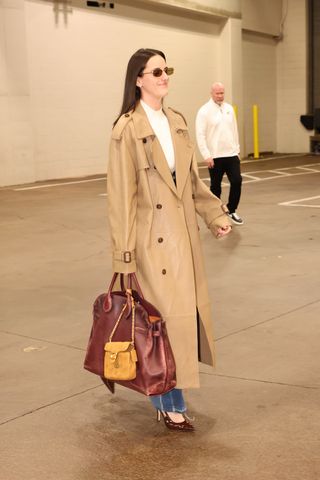 Caitlin Clark #22 of the Indiana Fever does a tunnel walk at the 2024 WNBA finals wearing a trench coat and jeans with a burgundy leather bag