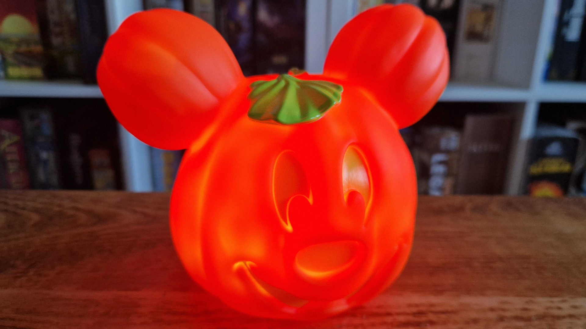 A Mickey Mouse pumpkin decoration on a wooden table, lit up and glowing