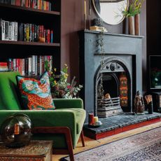 Living room with burgundy painted walls, fireplace, green armchair and vintage rug