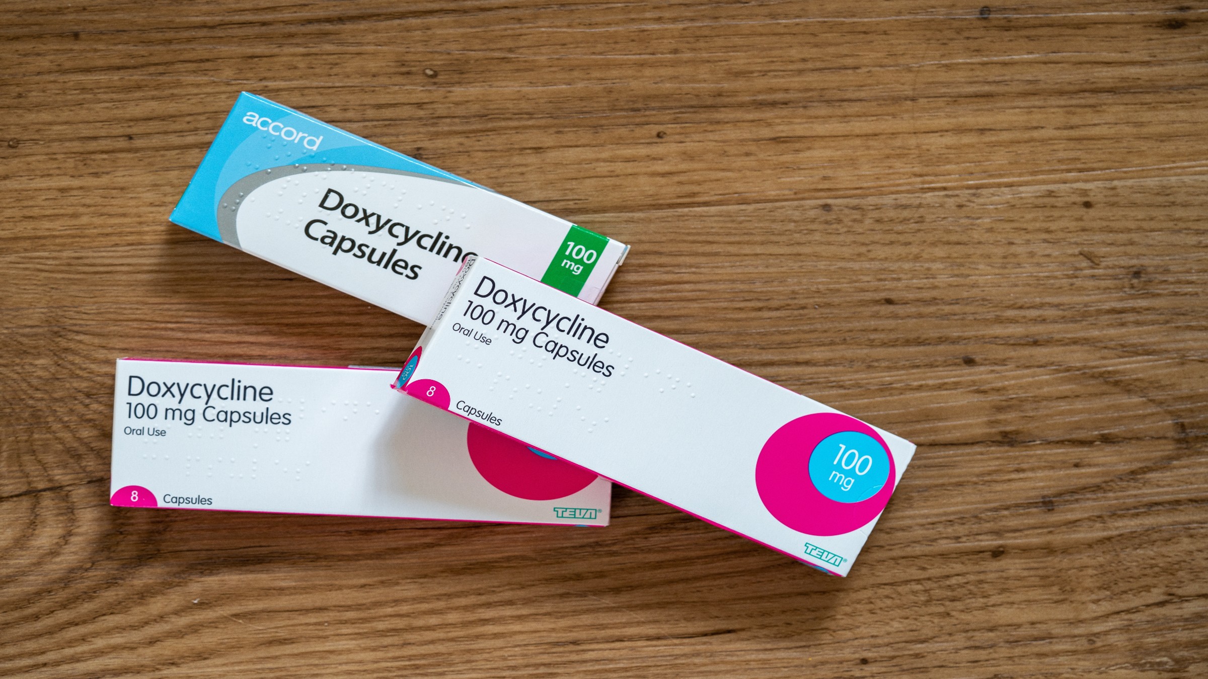 Three boxes of capsules of doxycycline on a wooden table