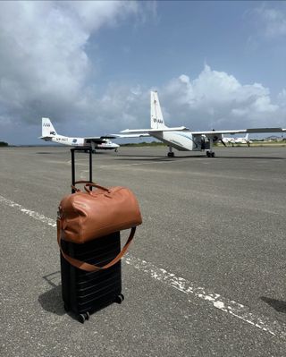 a leather Longchamp duffel bag and black Away suitcase at the airport