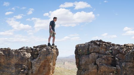 A man stands at a gap between two cliffs.