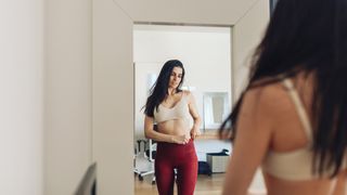 Woman in workout clothes looking at herself in mirror