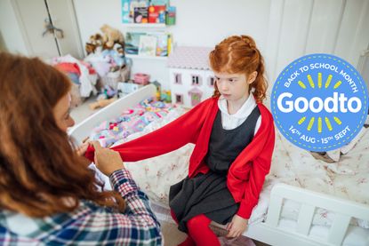 A medium shot of a mid adult, Caucasian mother trying to get her daughter to out her school cardigan on to get her ready for her first day of school. The girl is sat on the bed looking annoyed and displeased