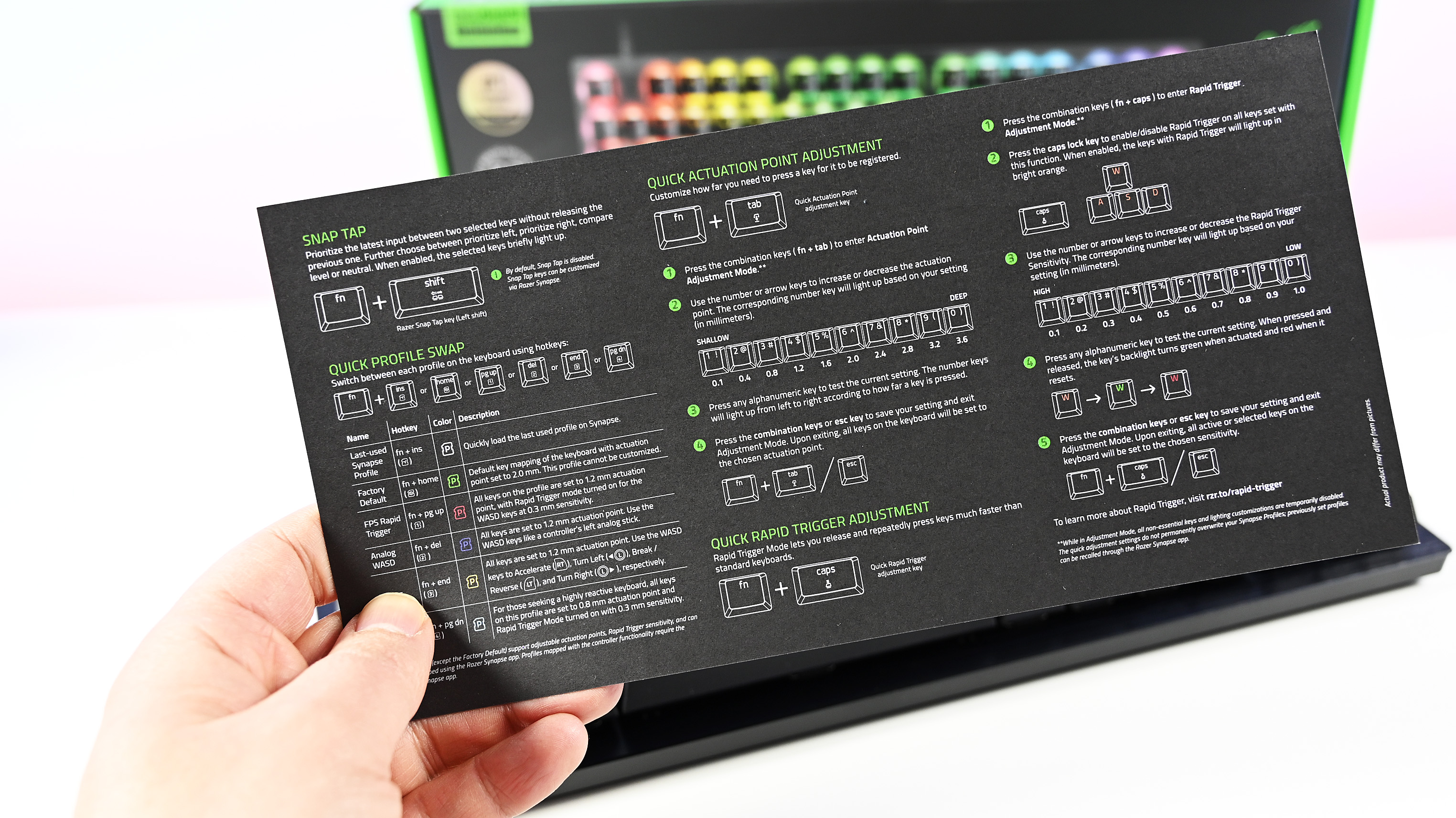 A hand holds a black Razer instruction manual with green text, detailing keyboard settings. A colorful keyboard is partially visible in the blurred background.