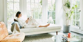 Woman relaxing on a chaise lounge in a white living room with white French doors to the garden beyond