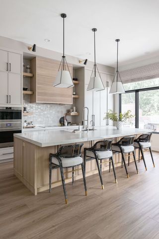 A kitchen with wooden cabinets and a large white island with three white cone-shaped pendant lights hanging overhead