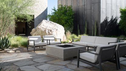 An outdoor minimalist garden space with white furniture, a fire pit, a large rock, and textured plants