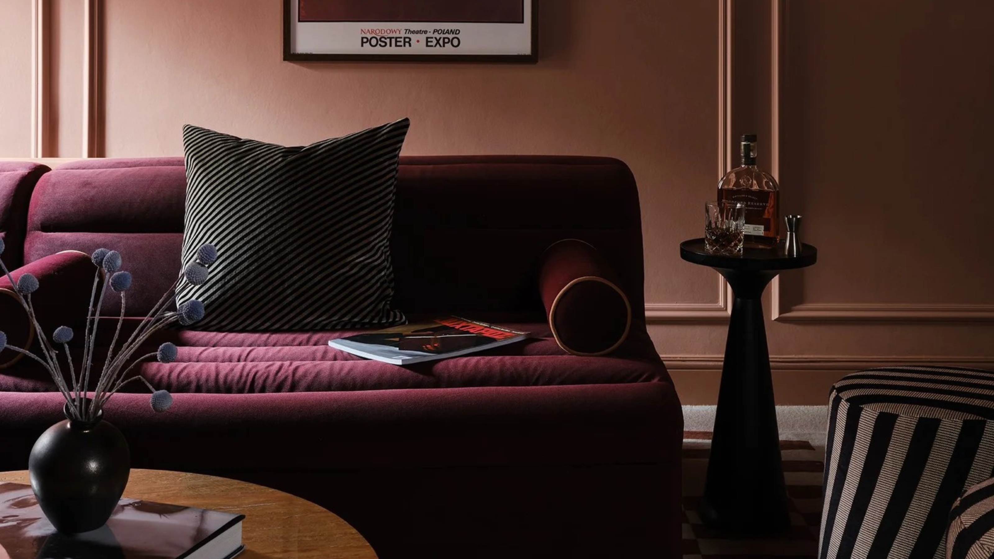 Image of a dark plum, purple sofa in a dark living room where the walls are painted in a dusty pink. There is a mini drinks table next to the sofa.