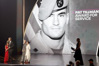 Prince Harry accepting the Pat Tillman Award for Service on stage with a large photo of Pat Tillman behind him