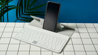 a google pixel phone propped up on a white, lightweight tablet keyboard made by mokibo rests upon a white tiled table with a blue background