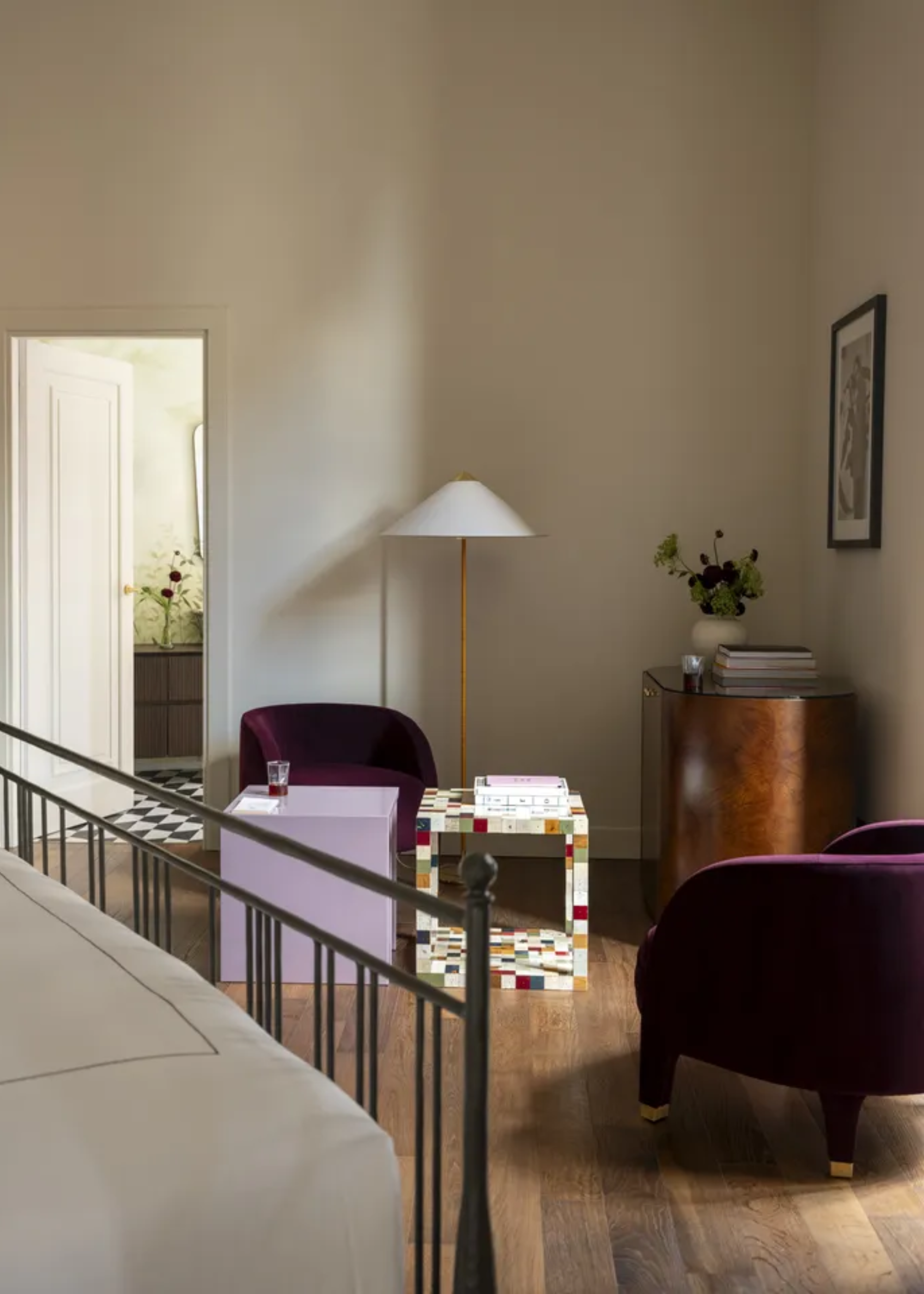 A simple bedroom with vibrant furniture in the form of color-cubed side tables, purple plush sofa seaters and framed art