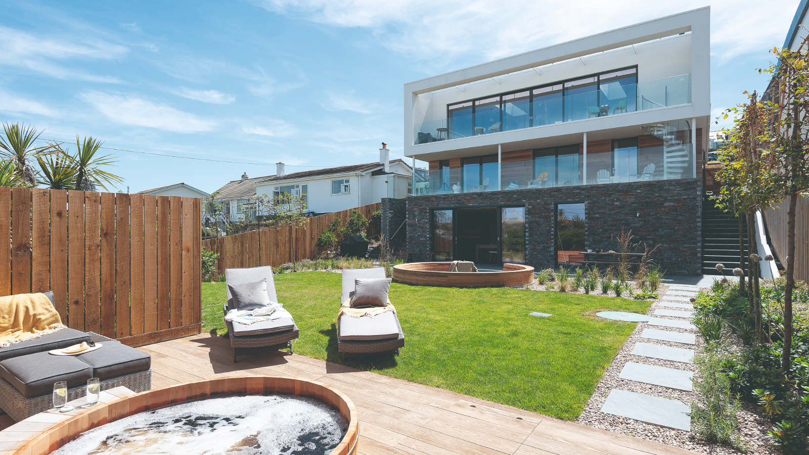 Exterior of the house, featuring the lawn, decking and hot tub with deck chairs