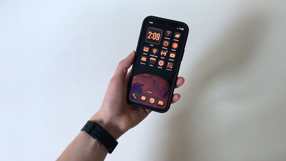 A person&#039;s hand holding an iPhone showing the iOS 18 home screen