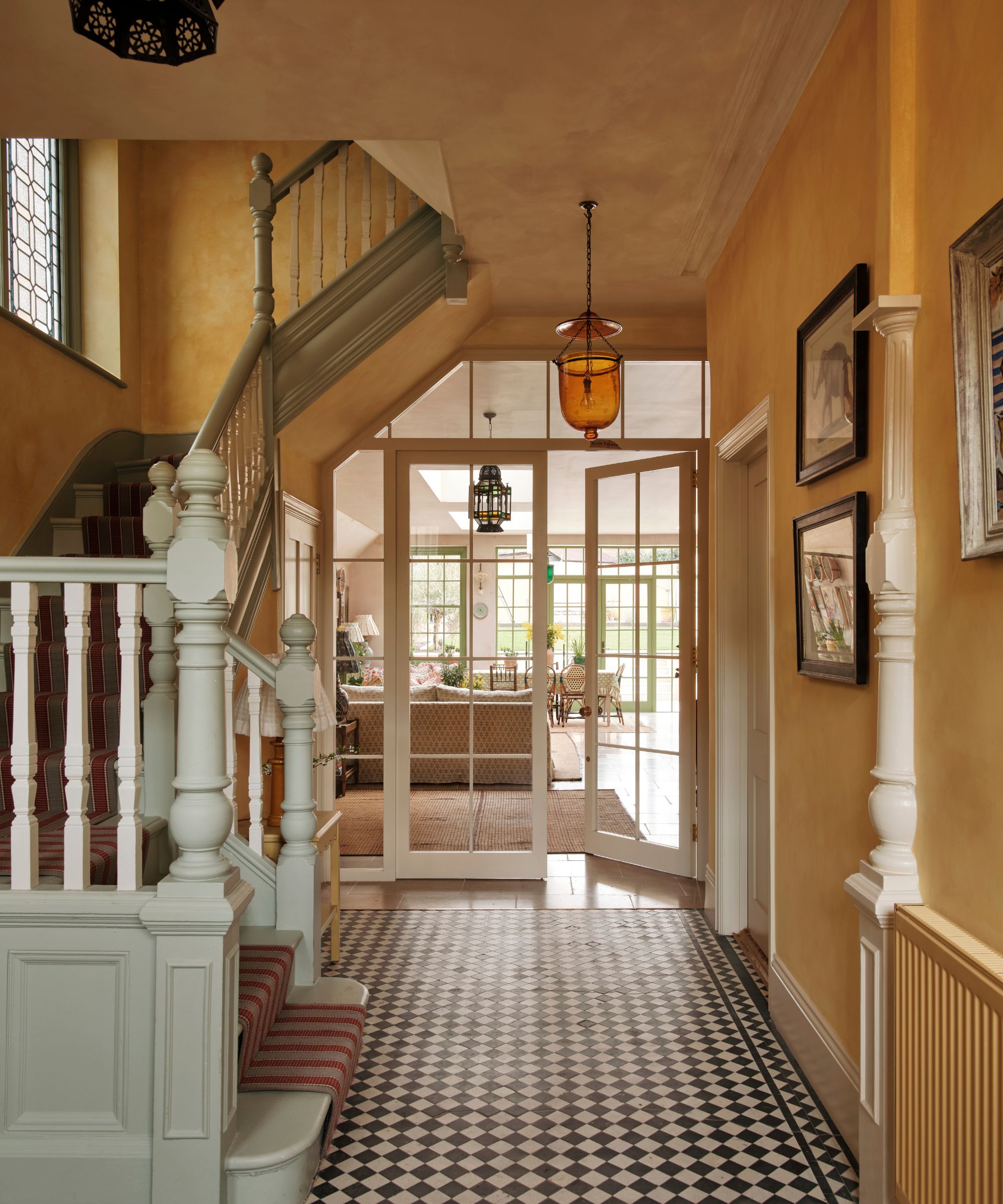 Hallway with yellow walls, wooden staircase painted pale blue, black and white tiled floor and glass french doors