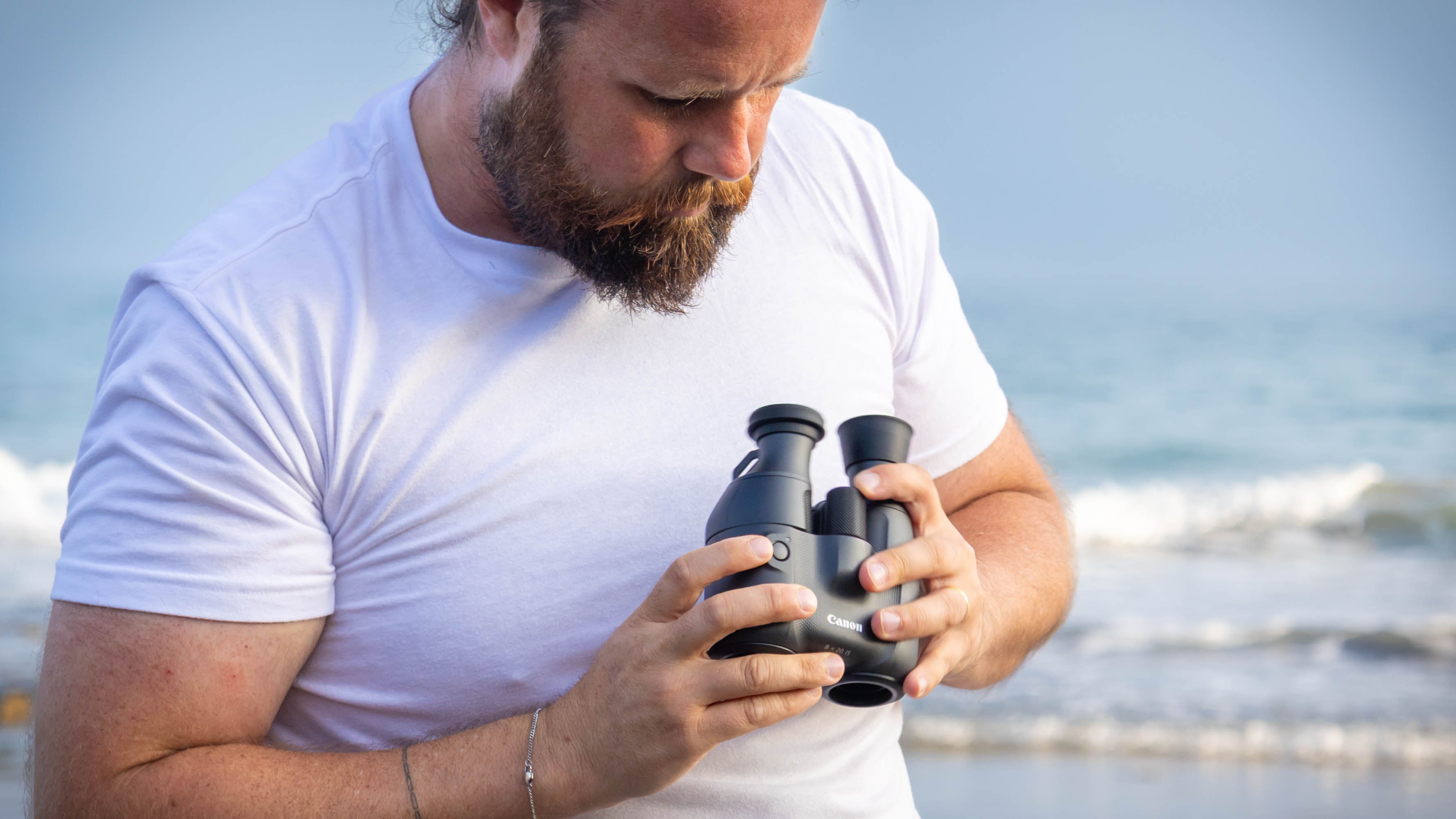 A male holding the Canon 8x20 IS binoculars with the sea behind them.