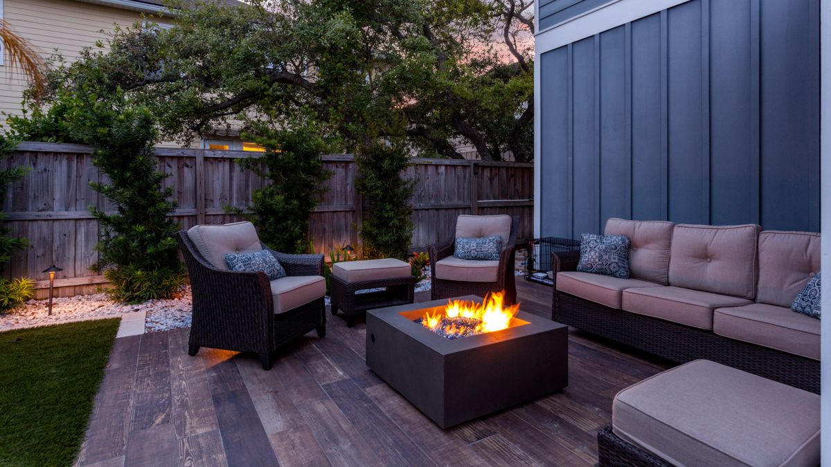 Patio furniture surrounding a lit firepit in a backyard