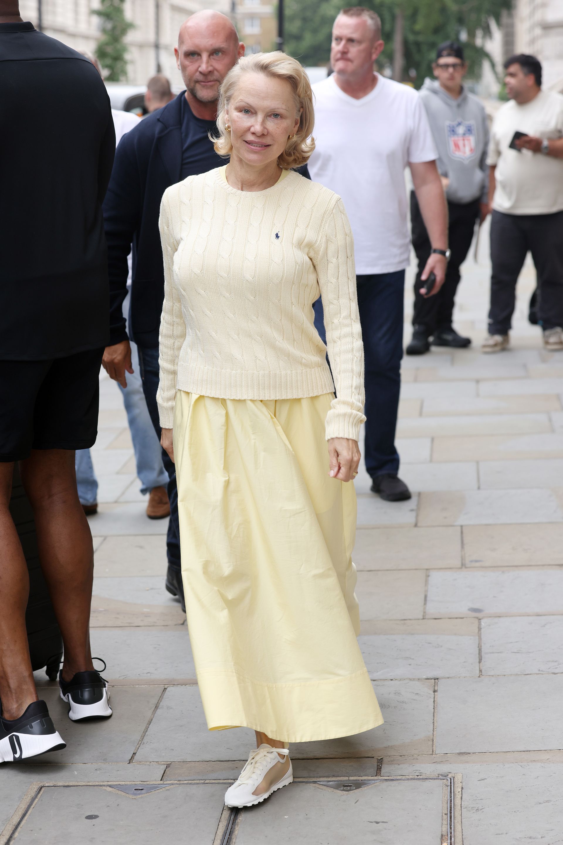 Pamela Anderson wears a yellow knit and yellow maxi skirt with white and gold trainers.